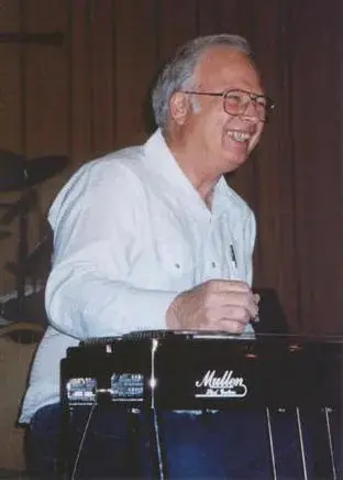 An older man smiling while playing a keyboard.