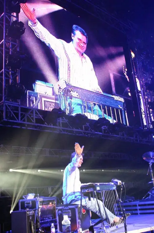 A man on stage with a large screen in front of him.